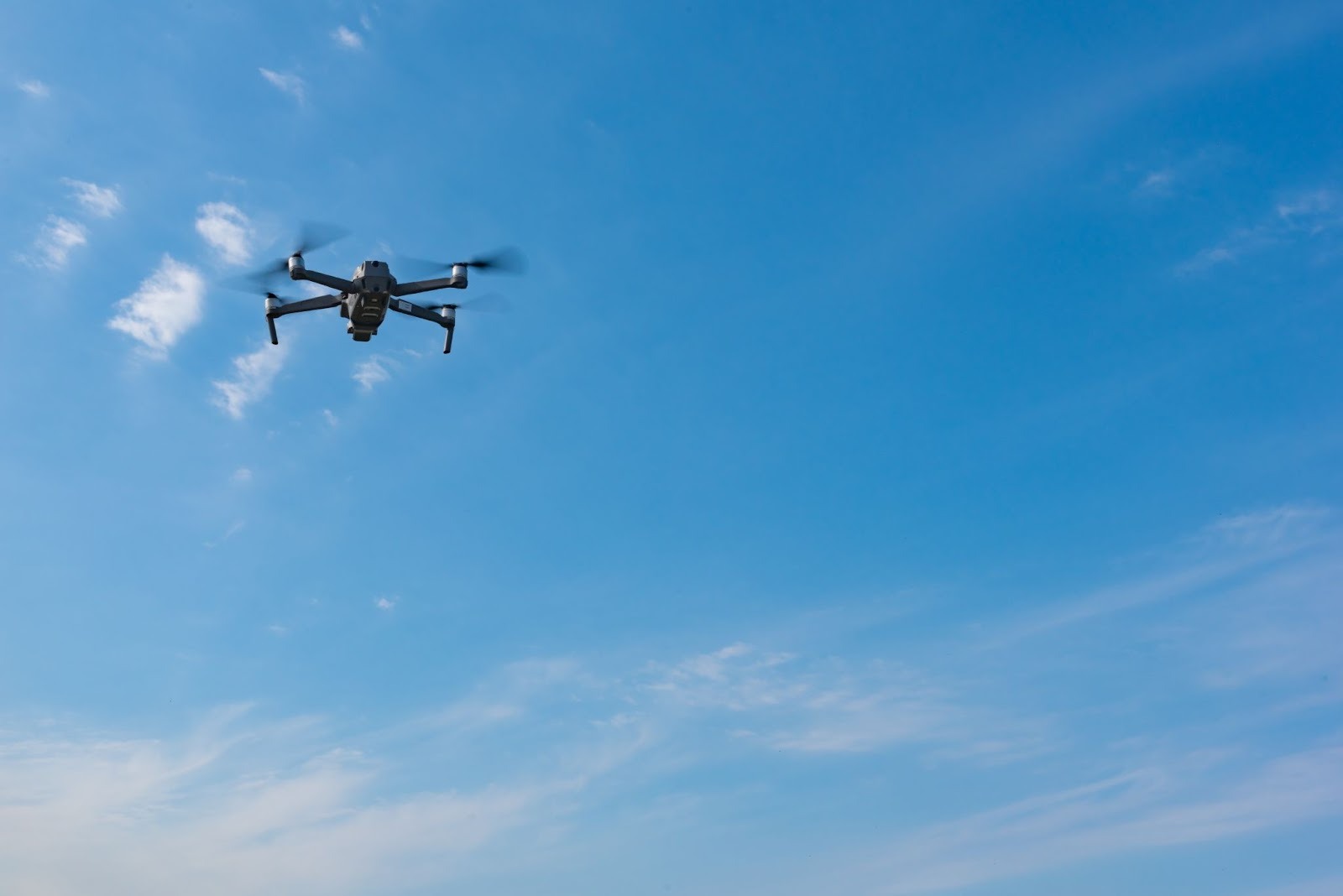 青空を飛行するドローンの写真。飛行距離や目視外飛行の限界を解説。